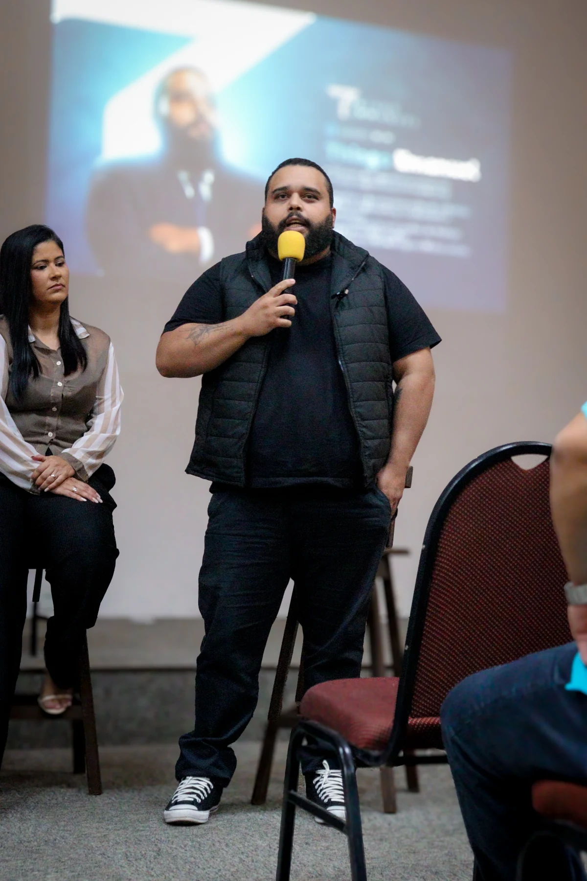Thiago falando ao microfone em uma apresentação, de corpo inteiro
